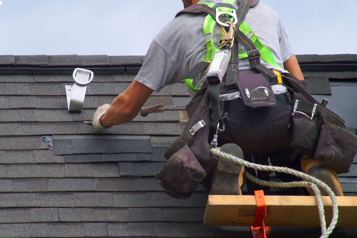 A man is engaged in roofing work, utilizing a ladder to reach the elevated area safely.