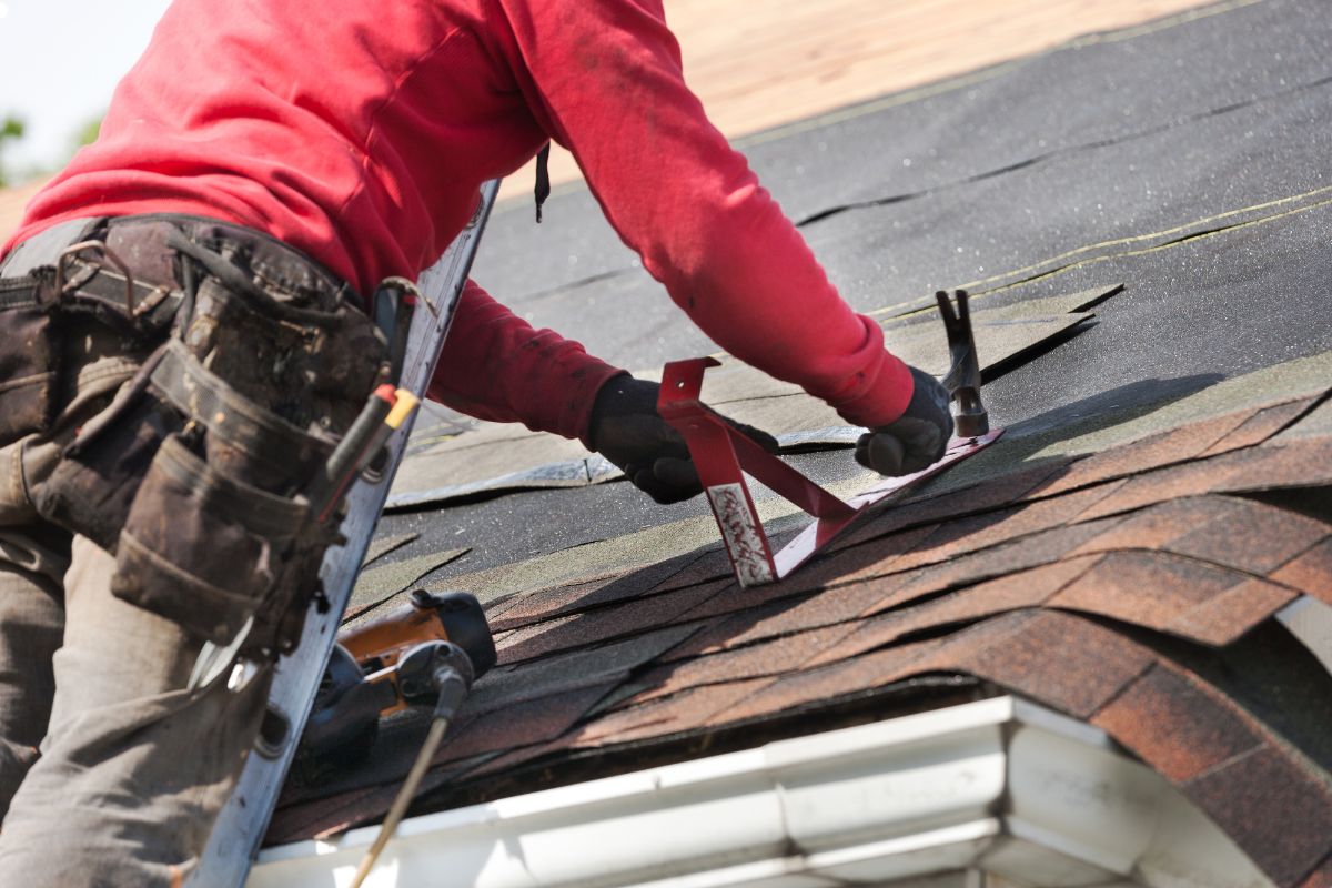 A man diligently works on a roof, employing a tool to complete his construction project.